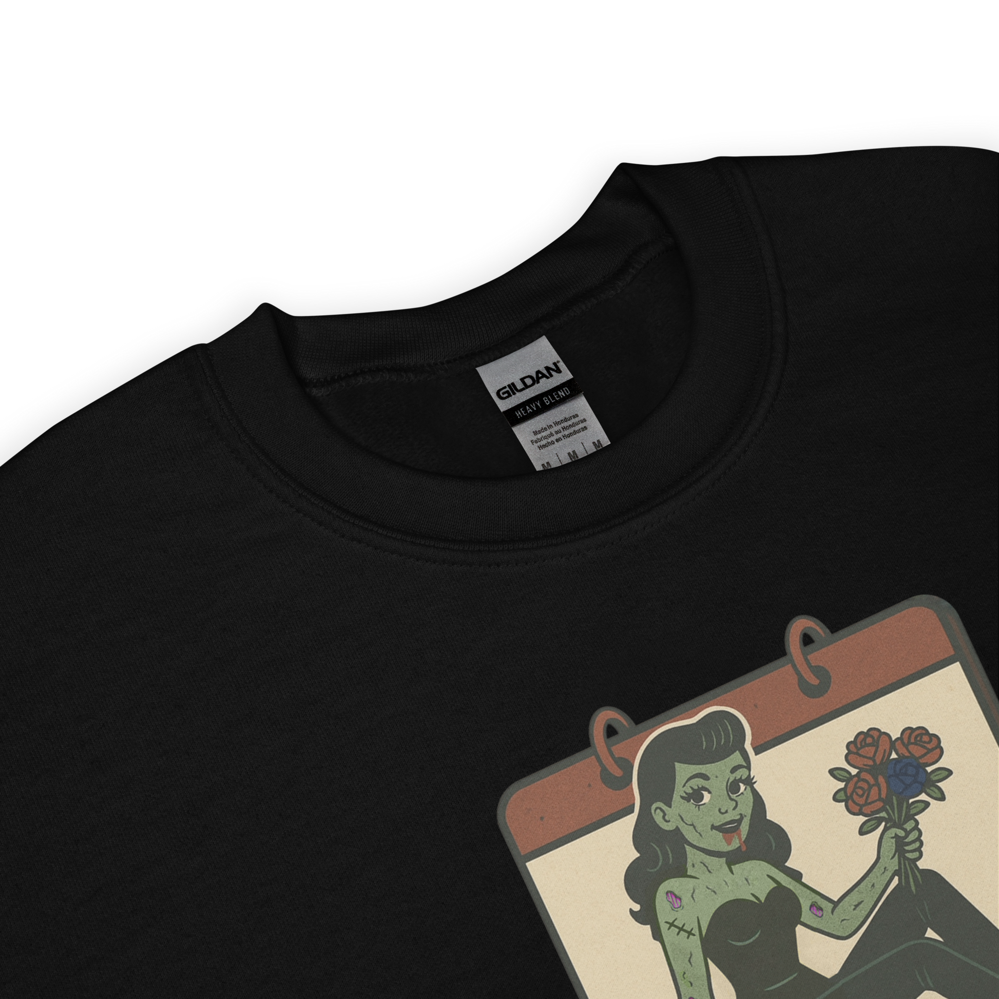 A black sweatshirt design with a vintage-style design on the front. The design features a green pinup-style zombie girl holding flowers, with a banner underneath that reads “CREEPY ALL YEAR.”