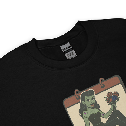 A black sweatshirt design with a vintage-style design on the front. The design features a green pinup-style zombie girl holding flowers, with a banner underneath that reads “CREEPY ALL YEAR.”