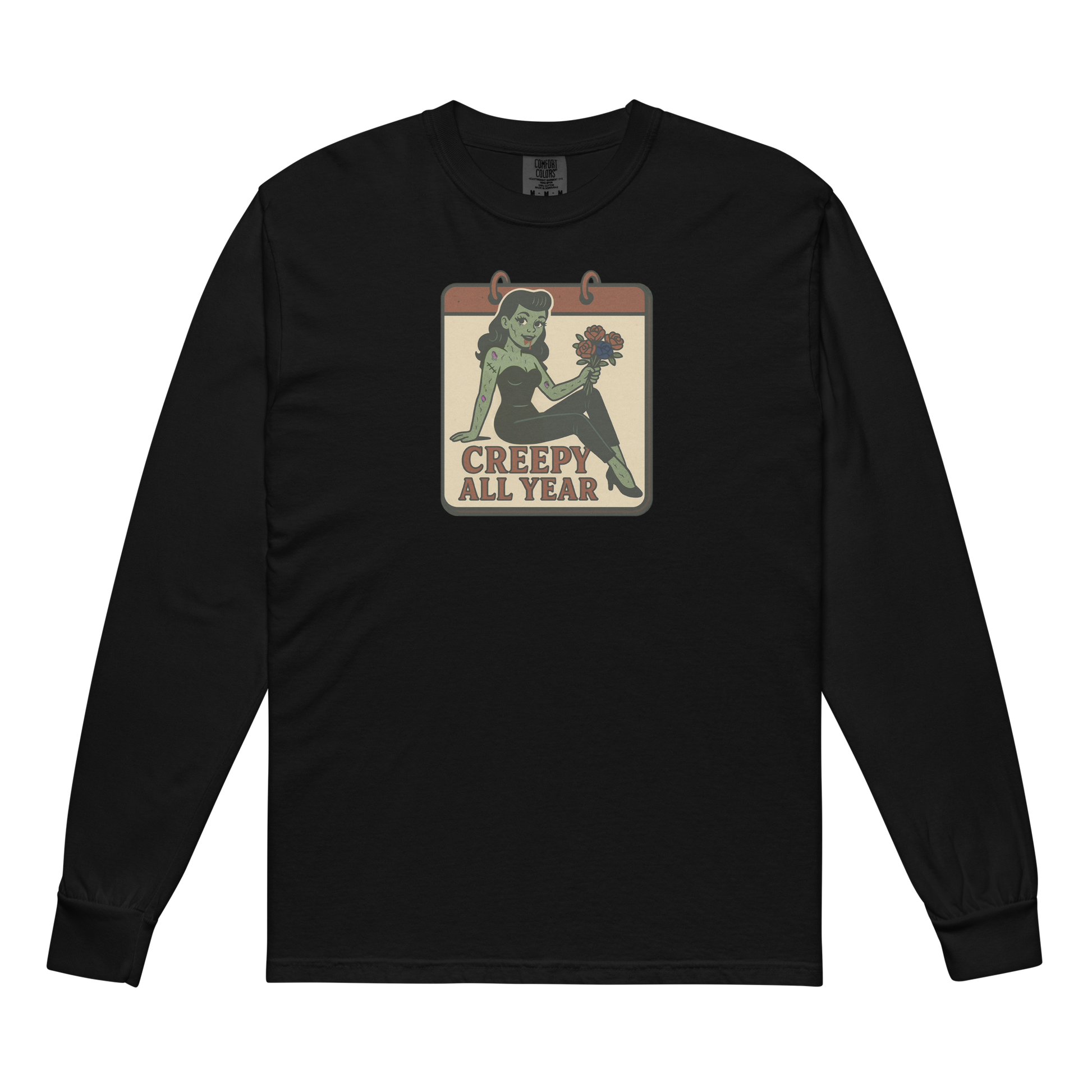 A black long sleeve t-shirt. The design features a green pinup-style zombie girl holding flowers, with a banner underneath that reads “CREEPY ALL YEAR.”