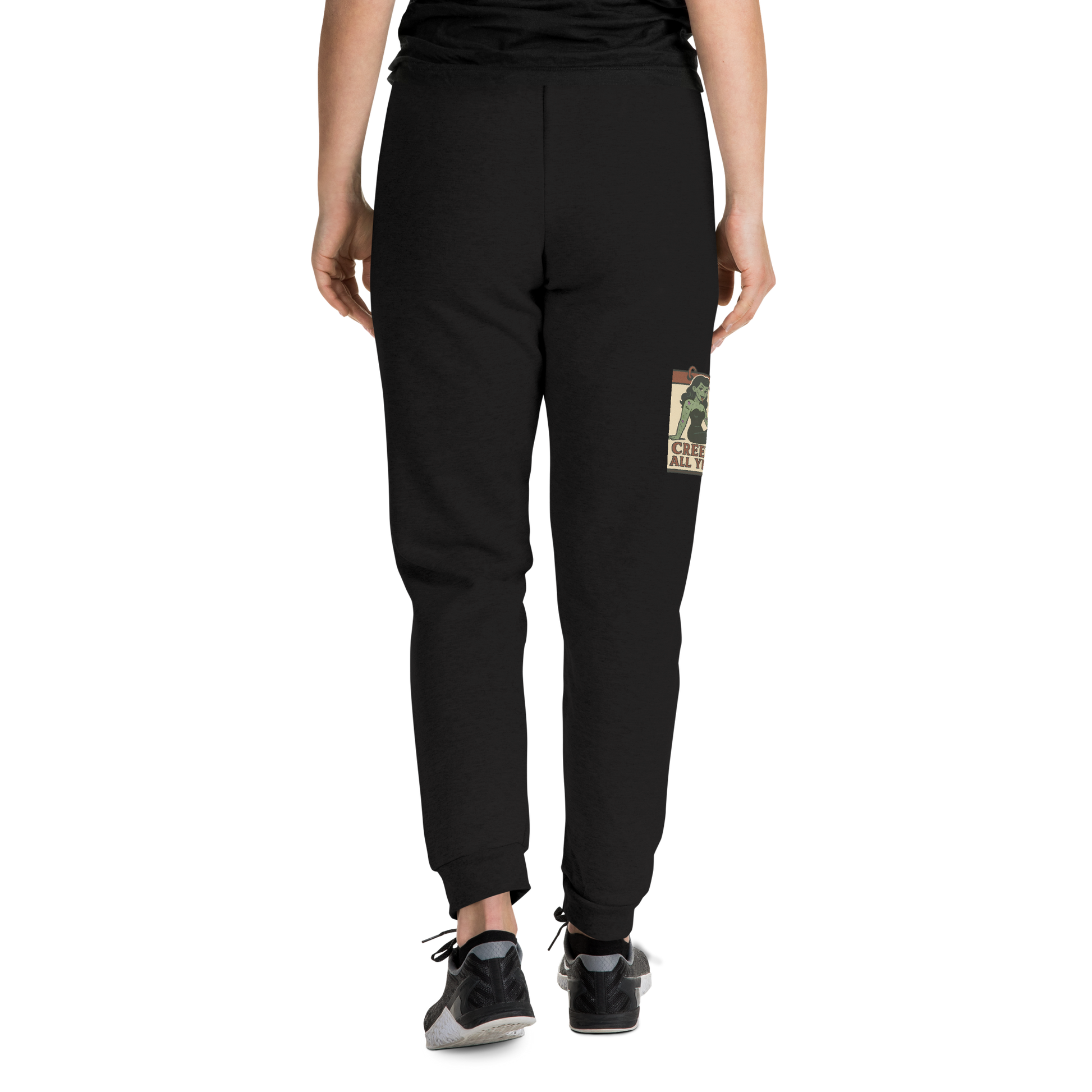 Back of black joggers on a girl with a black t-shirt, with a vintage-style design on the front. The design features a green pinup-style zombie girl holding flowers, with a banner underneath that reads “CREEPY ALL YEAR.”