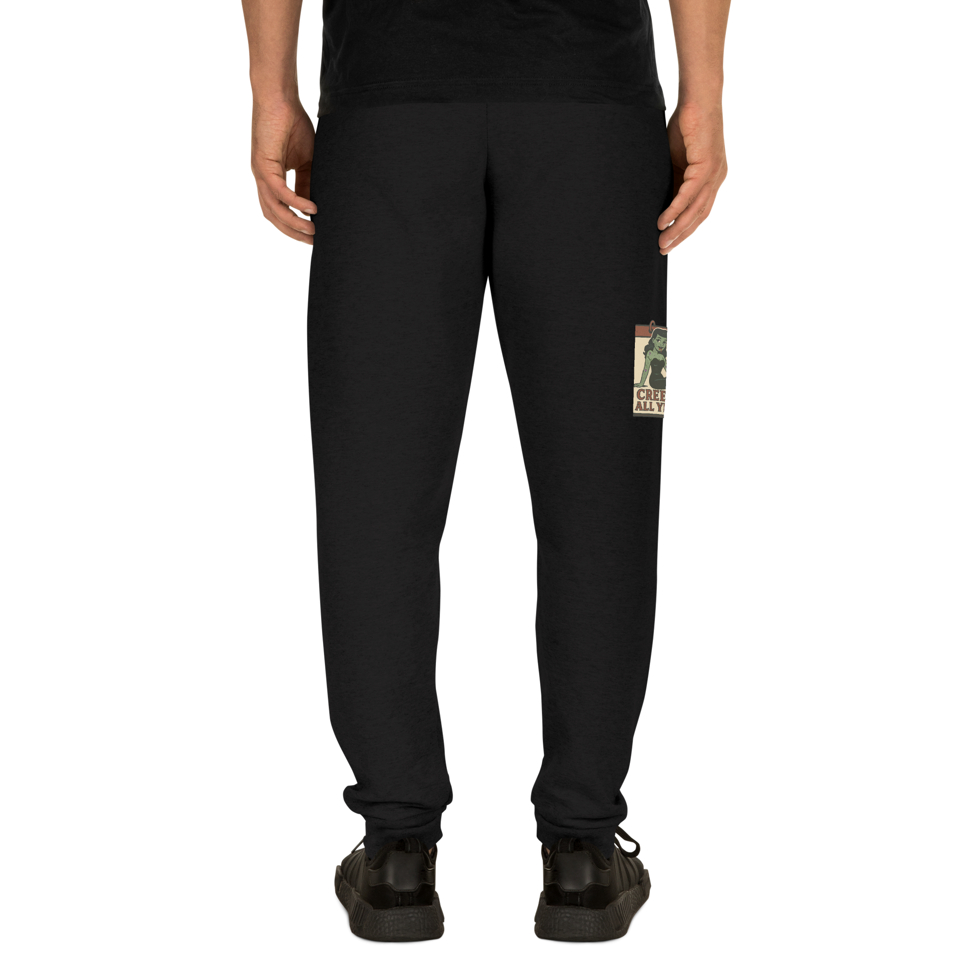 Back of black lack joggers on a man with a black t-shirt, with a vintage-style design on the front. The design features a green pinup-style zombie girl holding flowers, with a banner underneath that reads “CREEPY ALL YEAR.”