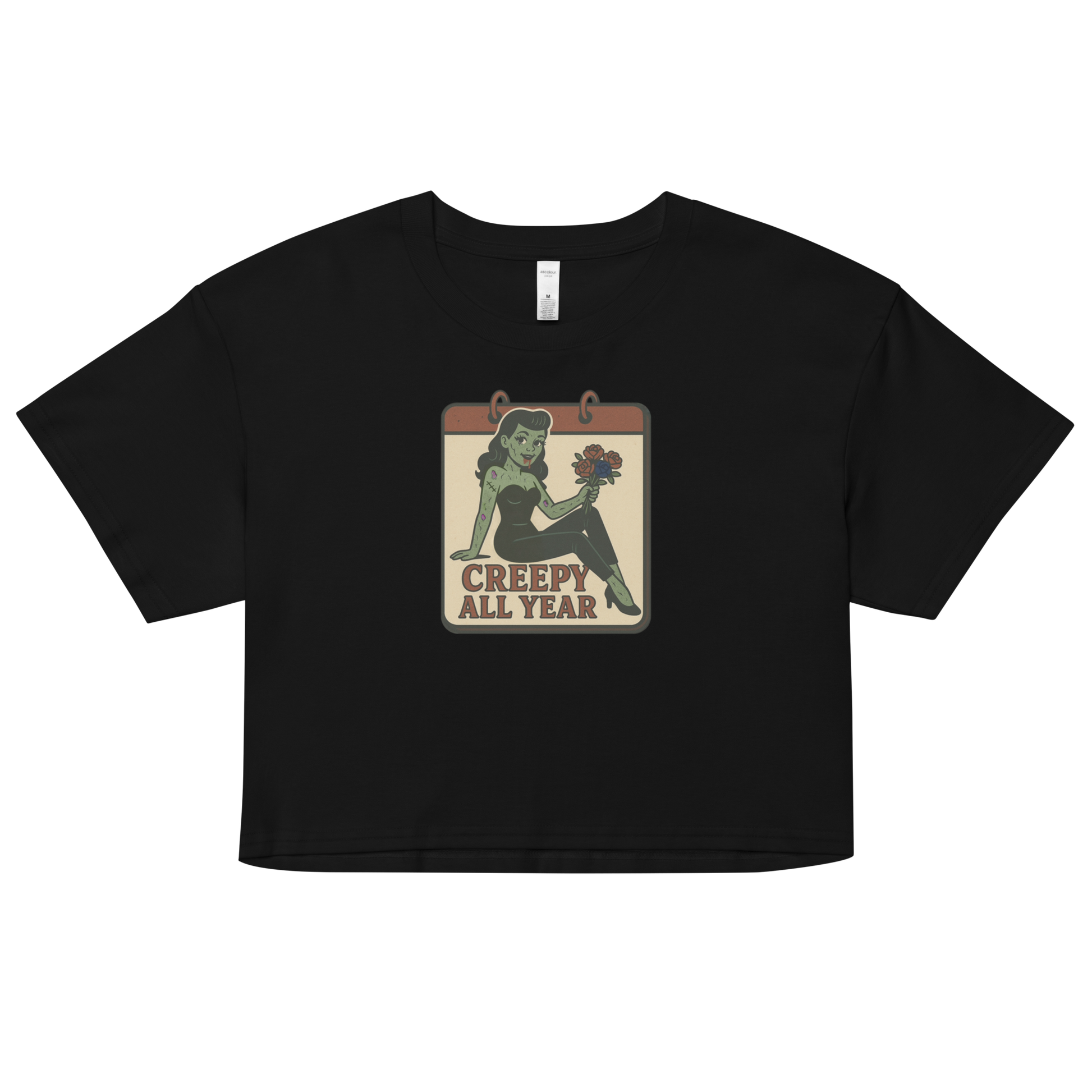 A black crop top with a vintage-style design on the front. The design features a green pinup-style zombie girl holding flowers, with a banner underneath that reads “CREEPY ALL YEAR.”