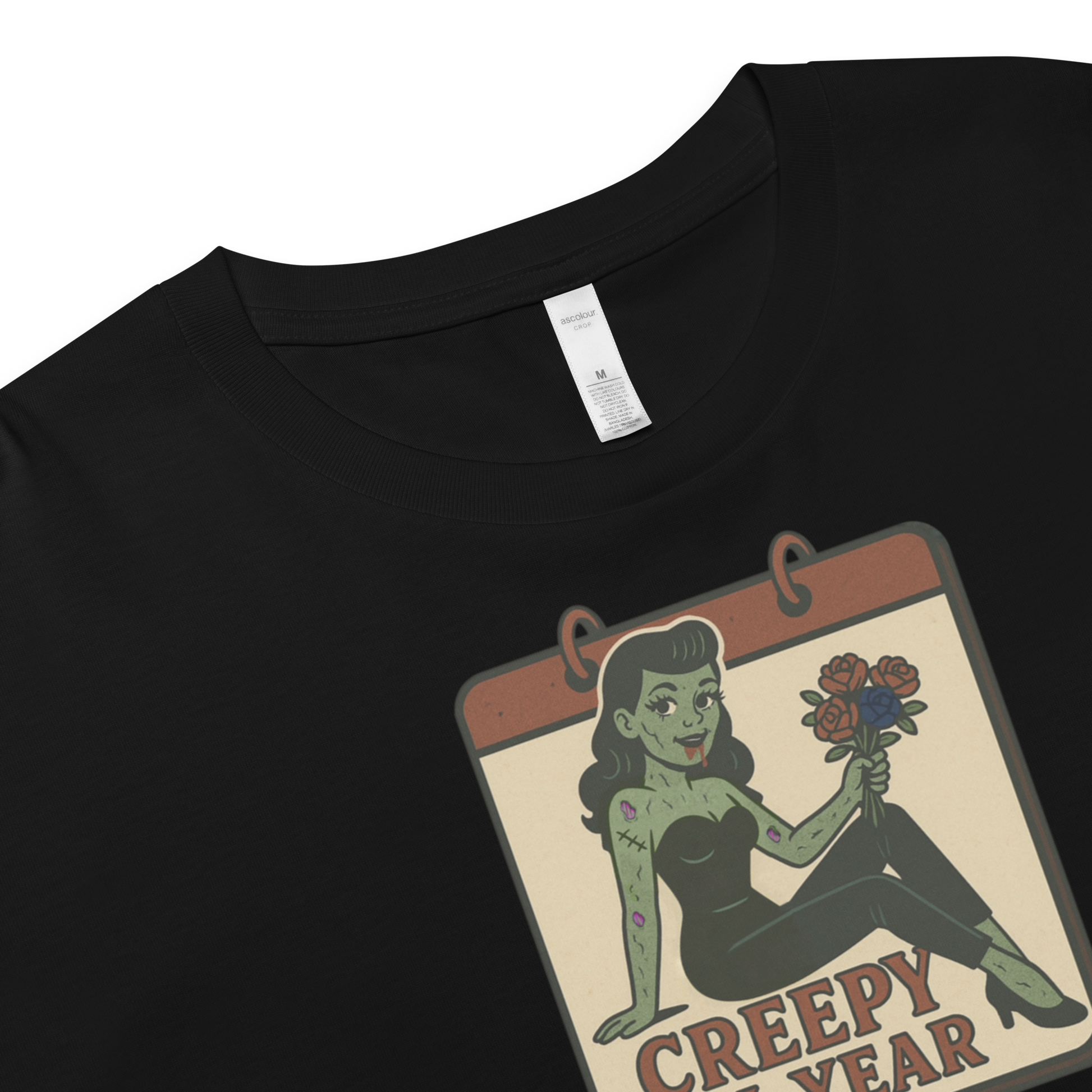 Black crop top with a graphic design of a pinup zombie holding flowers and 'Creepy All Year' text on a beige background.