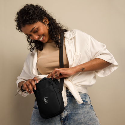 This is a woman with dark hair wearing a black crossbody bag that has a bored skeleton with his head resting in his hand and he has spider webs and bats around him and the text reads just waiting for October