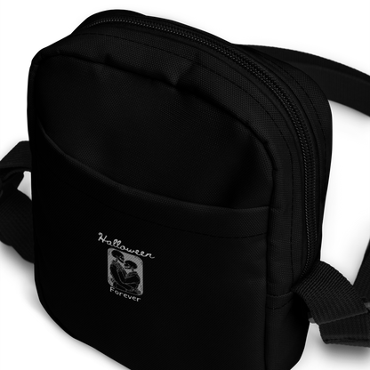This is a black crossbody bag that has a hugging skeleton couple that is grey and says Halloween Forever 