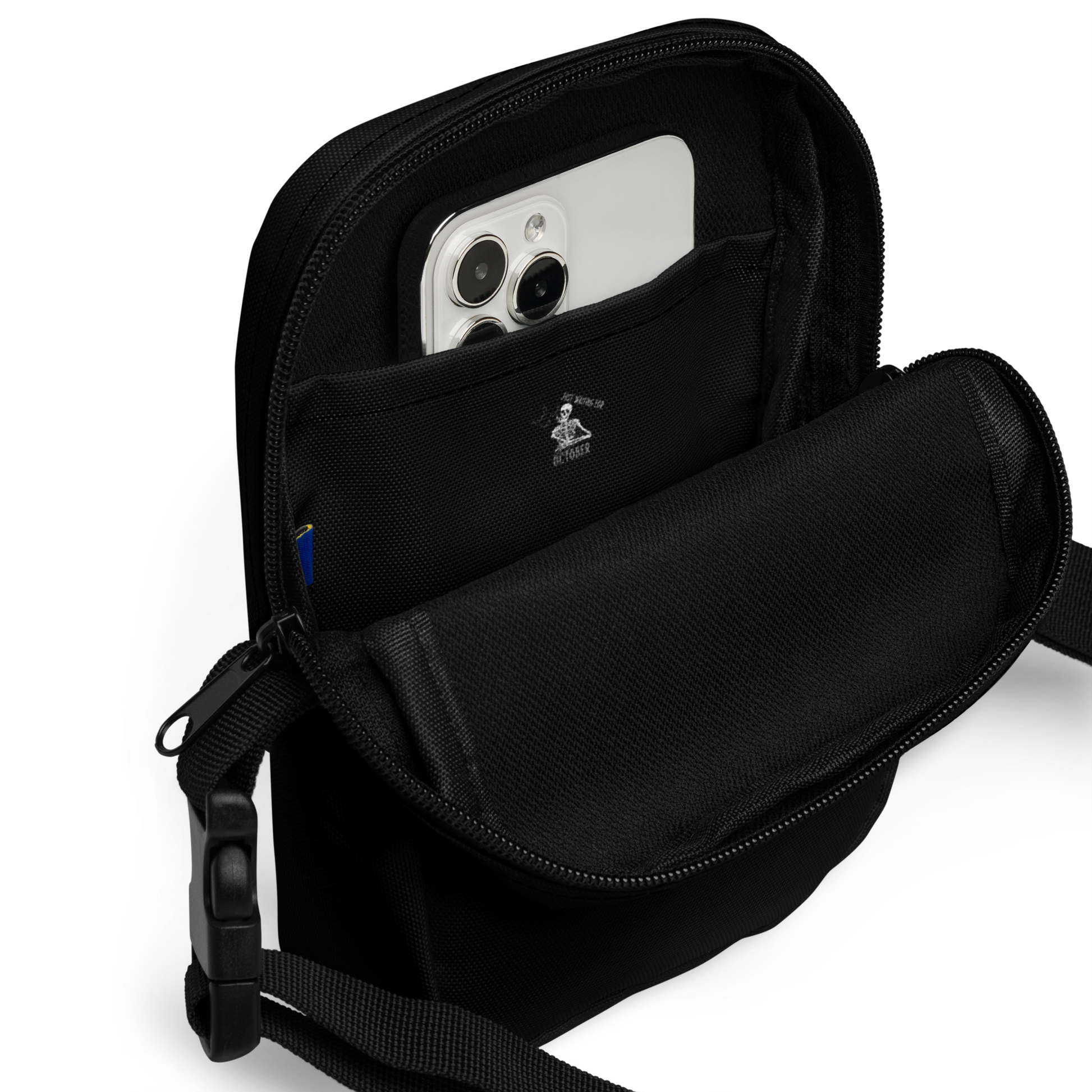 This is the inside of a black crossbody bag that has a bored skeleton with his head resting in his hand and he has spider webs and bats around him and the text reads just waiting for October