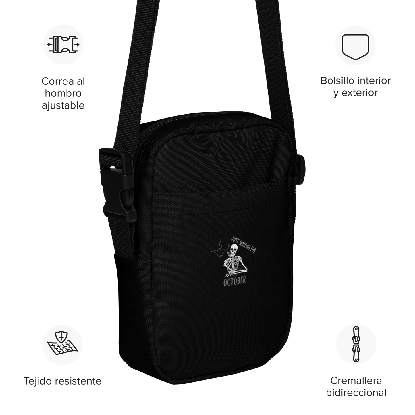 This is a black crossbody bag that has a bored skeleton with his head resting in his hand and he has spider webs and bats around him and the text reads just waiting for October