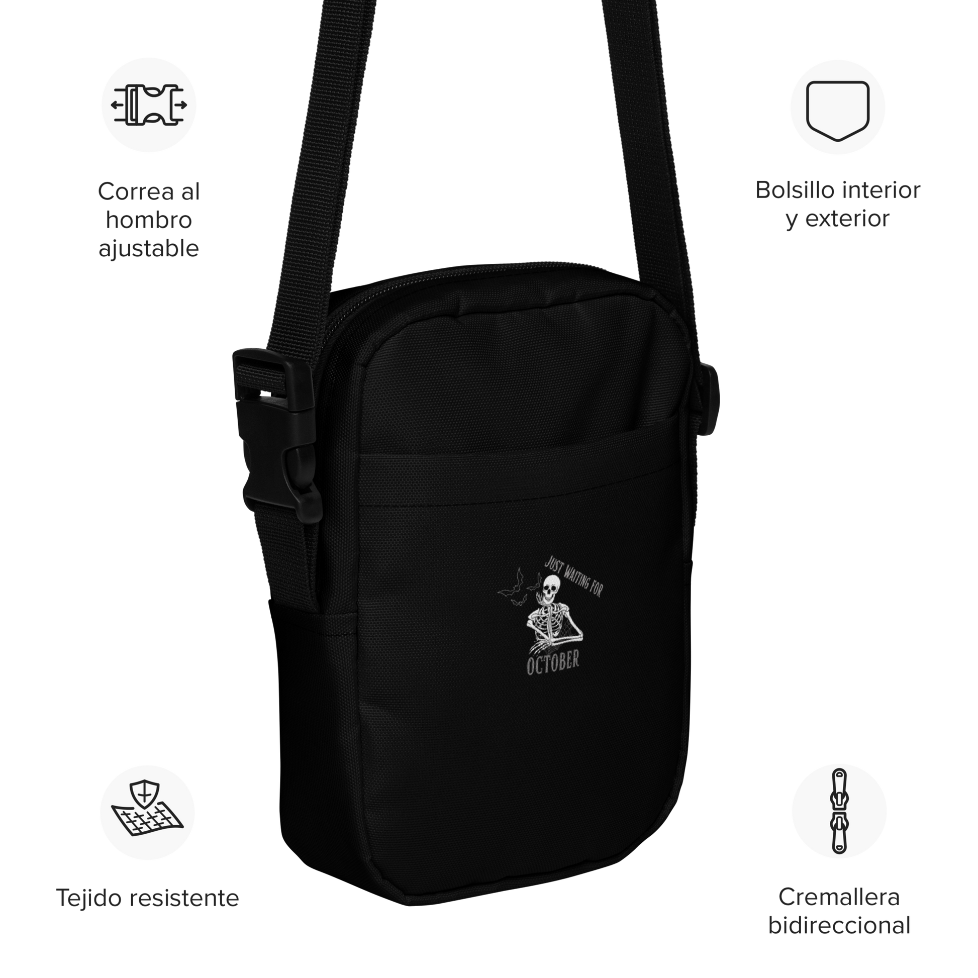 This is a black crossbody bag that has a bored skeleton with his head resting in his hand and he has spider webs and bats around him and the text reads just waiting for October