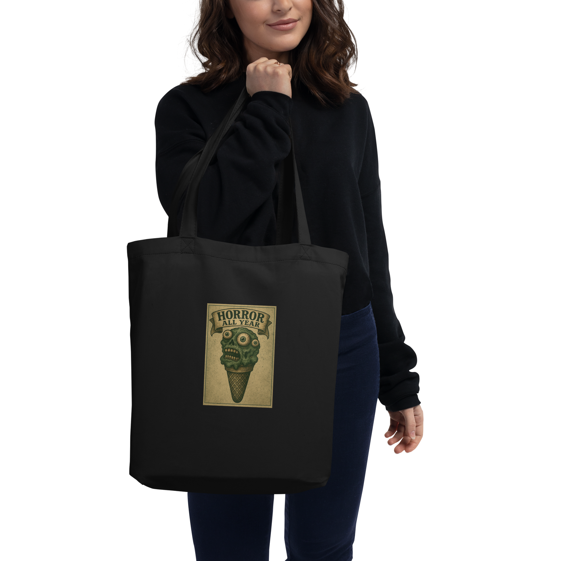 This is a woman with dark hair holding a black tote bag  that is a vintage-style illustration of a zombie-themed ice cream cone with a green, melting undead face and bulging eyeballs. Above the cone, a horror banner reads "Horror All Year" on a distressed parchment background