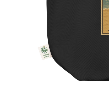 This is an organic tag of an eco tote bag with a retro-style illustration of a grinning skeleton lounging on a beach chair under an orange umbrella. The skeleton is holding a pumpkin-shaped drink cup with a straw and relaxing by the ocean, with a bright sun in the sky and a life preserver in the sand. The words “Creepy All Year” appear boldly at the top 