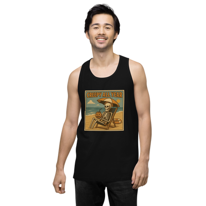 This is a man with dark hair wearing a black tank top with a retro-style illustration of a grinning skeleton lounging on a beach chair under an orange umbrella. The skeleton is holding a pumpkin-shaped drink cup with a straw and relaxing by the ocean, with a bright sun in the sky and a life preserver in the sand. The words “Creepy All Year” appear boldly at the top 