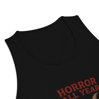 This is a zoom in of a black tank top with a cartoon illustration of a baby Baphomet goat with curved horns and a playful grin, wearing bright floral swim trunks while floating in a colorful inner tube. The character is set against a light background with the bold text “Horror All Year” above in red letters