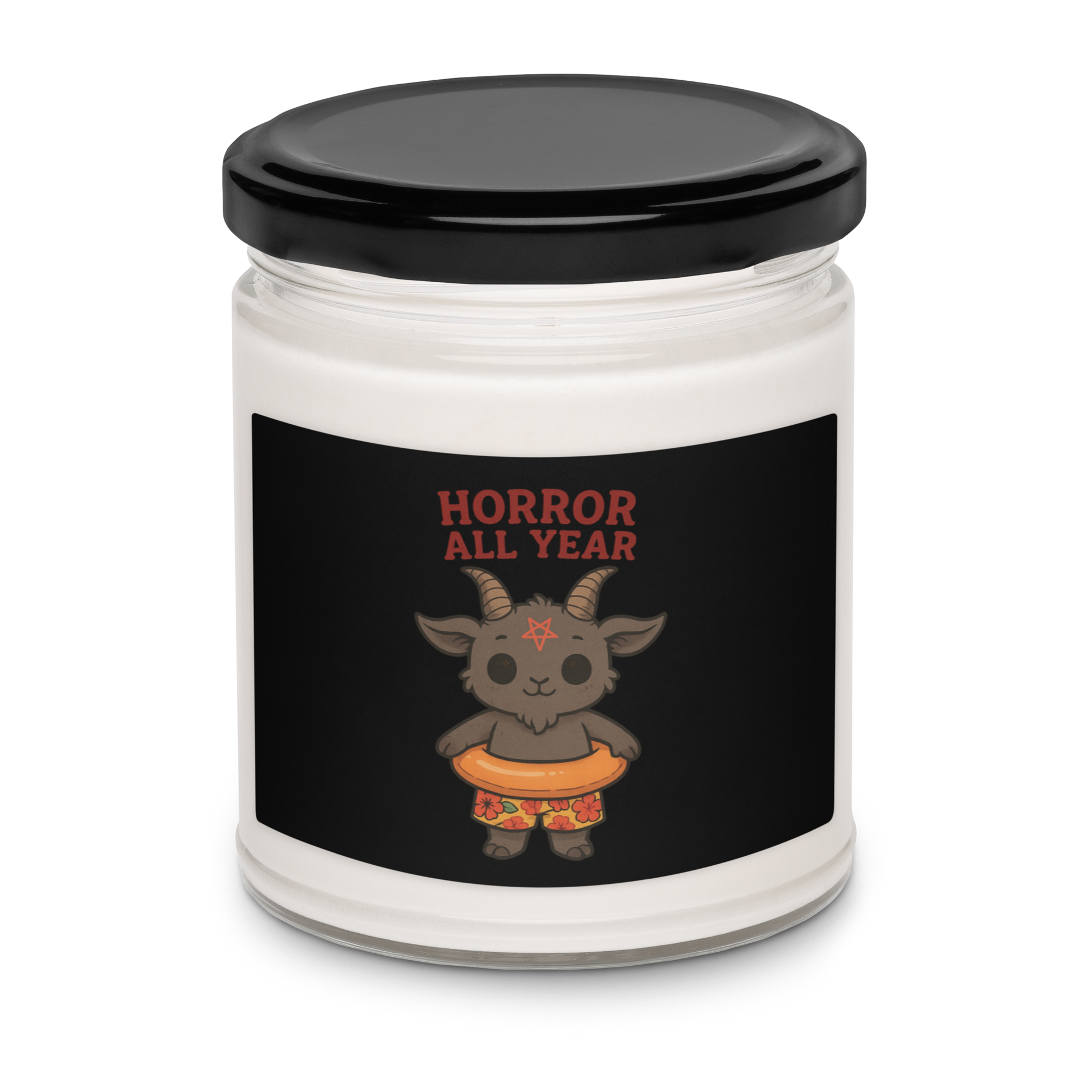 This is a white candle with a black tin lid on top and on the front is a cartoon illustration of a baby Baphomet goat with curved horns and a playful grin, wearing bright floral swim trunks while floating in a colorful inner tube. The character is set against a light background with the bold text “Horror All Year” above in red letters