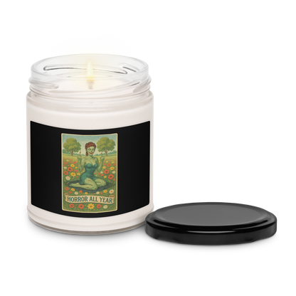 This is a candle with a black tin lid and a black label with a design illustration of a sassy zombie pinup girl standing in a floral field, wearing tattered lingerie and flipping off the viewer with both hands. She has green skin, vintage curls, and a bold attitude. The design blends horror and humor, with a pastel color palette and creepy cute vibes