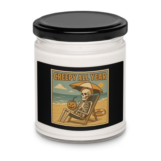 This is a white candle with black tin lid and black label with a retro-style illustration of a grinning skeleton lounging on a beach chair under an orange umbrella. The skeleton is holding a pumpkin-shaped drink cup with a straw and relaxing by the ocean, with a bright sun in the sky and a life preserver in the sand. The words “Creepy All Year” appear boldly at the top 