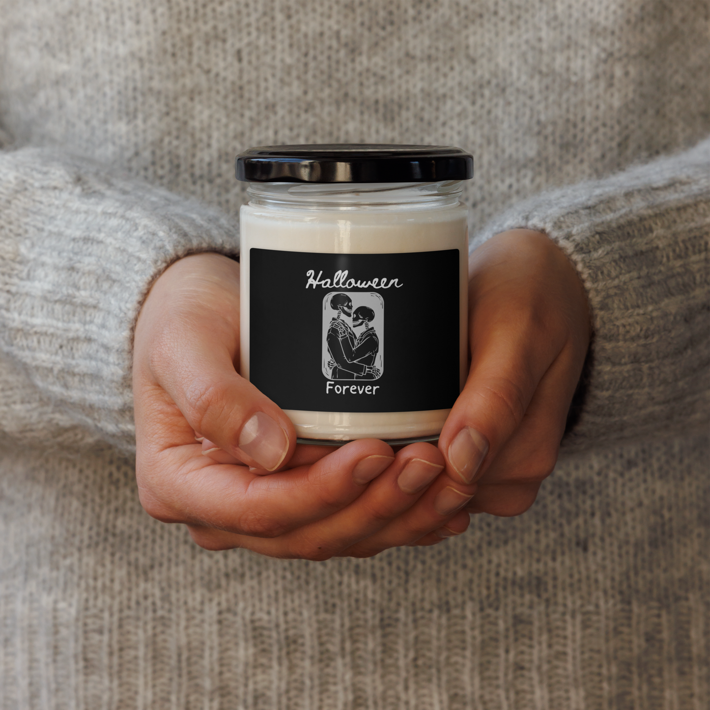 This is a woman holding a candle with a black label that has a hugging skeleton couple that is grey and says Halloween Forever 