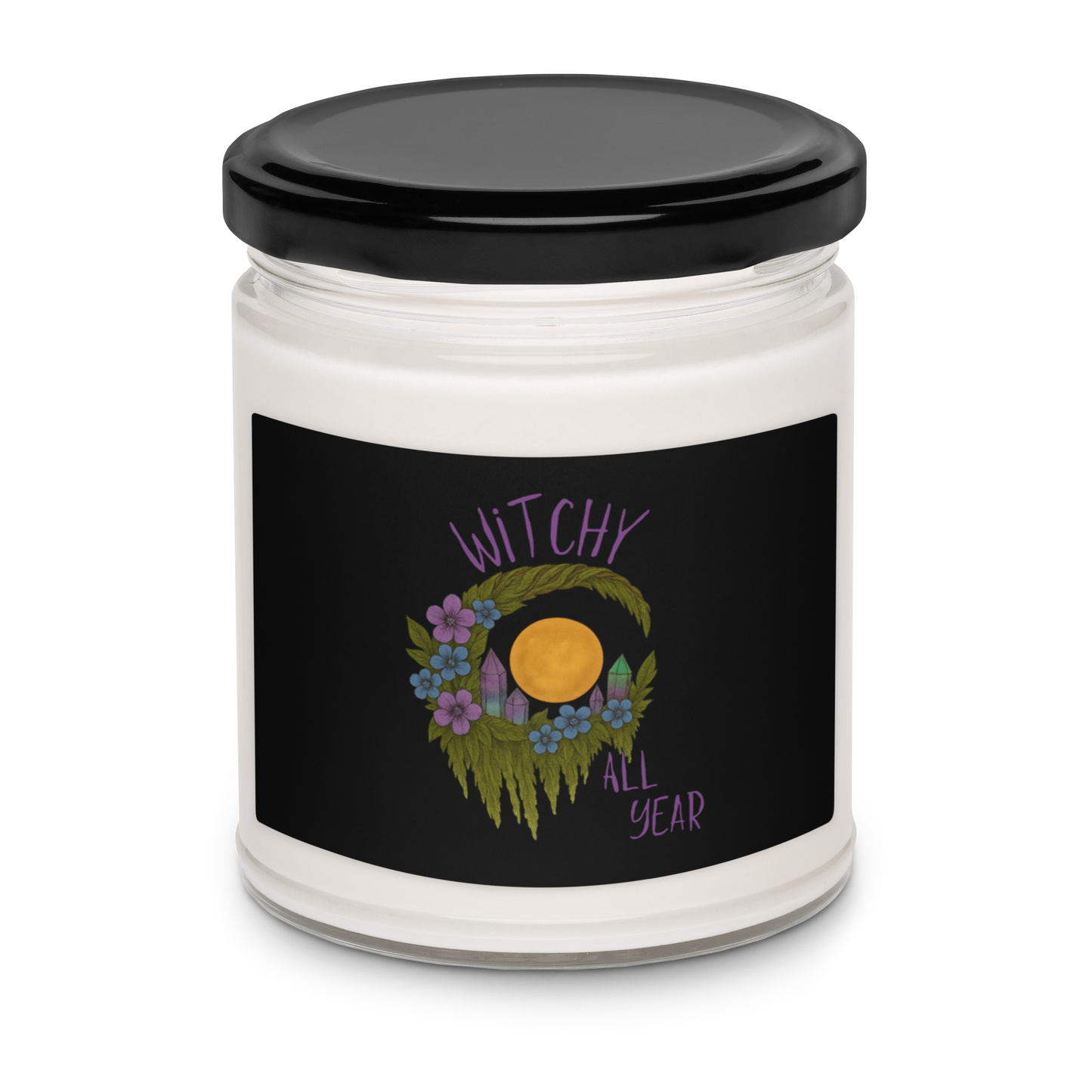 This is a white candle with a design of a hand-drawn wreath made of moss-covered branches wraps around a glowing sun. The wreath is decorated with purple and blue flowers, small amethyst and fluorite crystals, and strands of hanging moss. The words “Witchy” curve above the wreath and “All Year” sits on the bottom right 