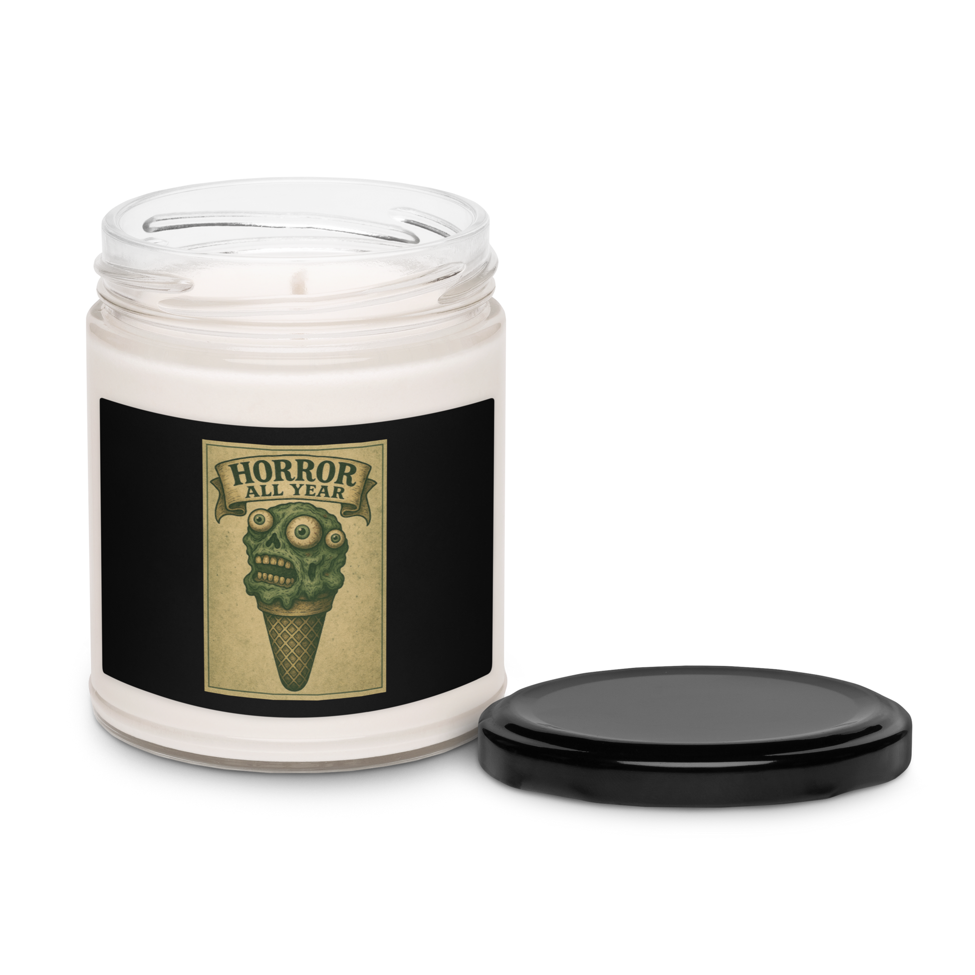 This is a candle with black tin lid and  black label that is a vintage-style illustration of a zombie-themed ice cream cone with a green, melting undead face and bulging eyeballs. Above the cone, a horror banner reads "Horror All Year" on a distressed parchment background