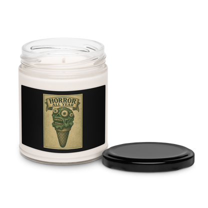 This is a candle with black tin lid and  black label that is a vintage-style illustration of a zombie-themed ice cream cone with a green, melting undead face and bulging eyeballs. Above the cone, a horror banner reads "Horror All Year" on a distressed parchment background