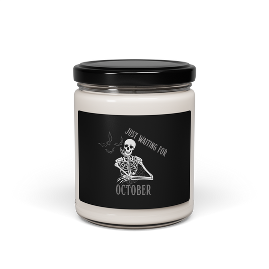 This is a white candle with black label that has a bored skeleton with his head resting in his hand and he has spider webs and bats around him and the text reads just waiting for October