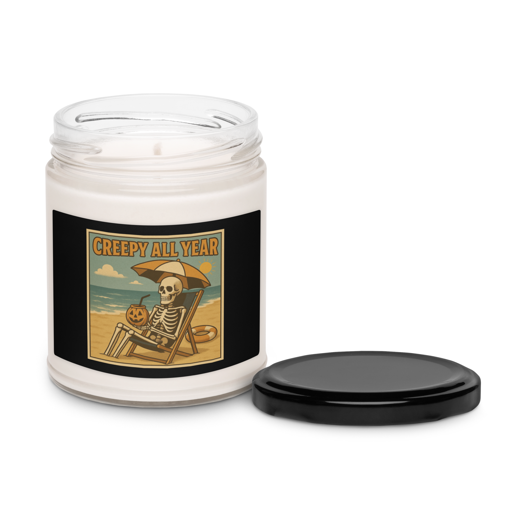 This is a white candle with black tin lid and black label with a retro-style illustration of a grinning skeleton lounging on a beach chair under an orange umbrella. The skeleton is holding a pumpkin-shaped drink cup with a straw and relaxing by the ocean, with a bright sun in the sky and a life preserver in the sand. The words “Creepy All Year” appear boldly at the top 