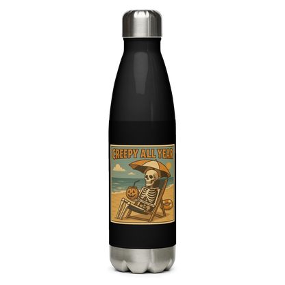 This is a black stainless steel water bottle with a retro-style illustration of a grinning skeleton lounging on a beach chair under an orange umbrella. The skeleton is holding a pumpkin-shaped drink cup with a straw and relaxing by the ocean, with a bright sun in the sky and a life preserver in the sand. The words “Creepy All Year” appear boldly at the top on the front side