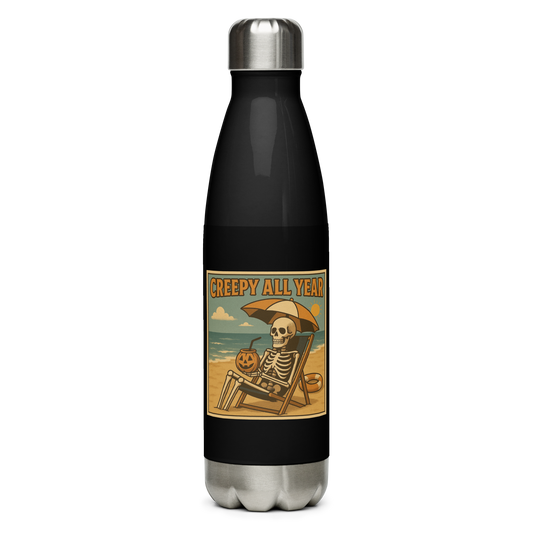 This is a black stainless steel water bottle with a retro-style illustration of a grinning skeleton lounging on a beach chair under an orange umbrella. The skeleton is holding a pumpkin-shaped drink cup with a straw and relaxing by the ocean, with a bright sun in the sky and a life preserver in the sand. The words “Creepy All Year” appear boldly at the top on the front side