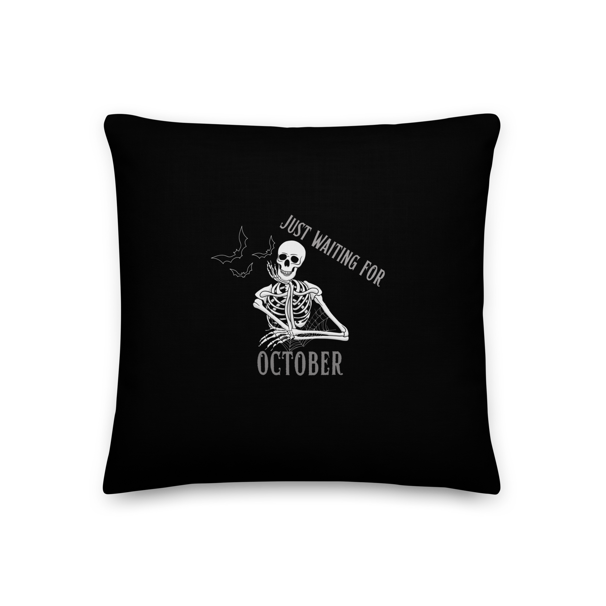 This is a black throw pillow that has a bored skeleton with his head resting in his hand and he has spider webs and bats around him and the text reads just waiting for October