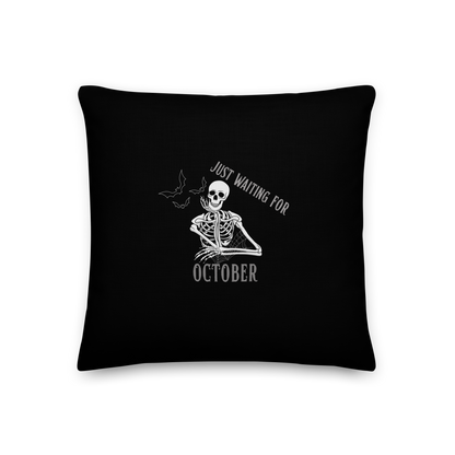 This is a black throw pillow that has a bored skeleton with his head resting in his hand and he has spider webs and bats around him and the text reads just waiting for October
