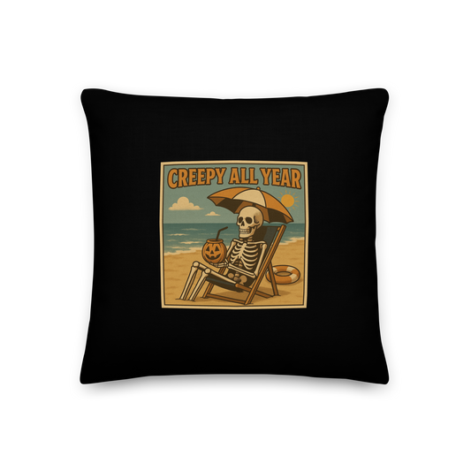 This is a black throw pillow with a retro-style illustration of a grinning skeleton lounging on a beach chair under an orange umbrella. The skeleton is holding a pumpkin-shaped drink cup with a straw and relaxing by the ocean, with a bright sun in the sky and a life preserver in the sand. The words “Creepy All Year” appear boldly at the top 