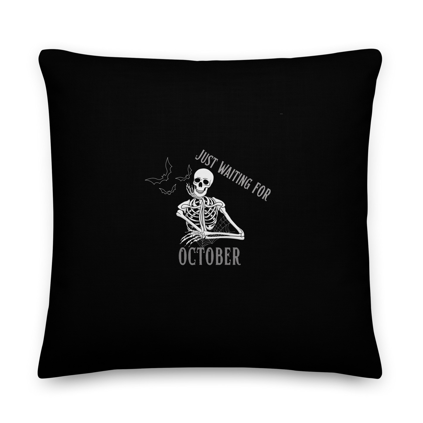This is a black throw pillow that has a bored skeleton with his head resting in his hand and he has spider webs and bats around him and the text reads just waiting for October