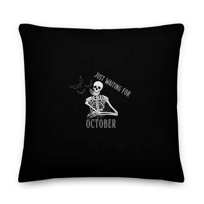 This is a black throw pillow that has a bored skeleton with his head resting in his hand and he has spider webs and bats around him and the text reads just waiting for October
