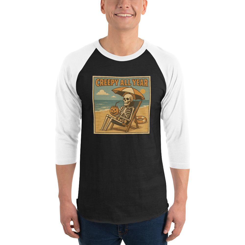 This is a man wearing a black and white raglan shirt with a retro-style illustration of a grinning skeleton lounging on a beach chair under an orange umbrella. The skeleton is holding a pumpkin-shaped drink cup with a straw and relaxing by the ocean, with a bright sun in the sky and a life preserver in the sand. The words “Creepy All Year” appear boldly at the top