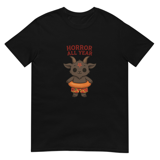 This is a black t-shirt with a cartoon illustration of a baby Baphomet goat with curved horns and a playful grin, wearing bright floral swim trunks while floating in a colorful inner tube. The character is set against a light background with the bold text “Horror All Year” above in red letters