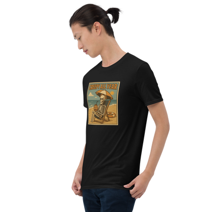This is a man with dark hair wearing a black t-shirt with a retro-style illustration of a grinning skeleton lounging on a beach chair under an orange umbrella. The skeleton is holding a pumpkin-shaped drink cup with a straw and relaxing by the ocean, with a bright sun in the sky and a life preserver in the sand. The words “Creepy All Year” appear boldly at the top