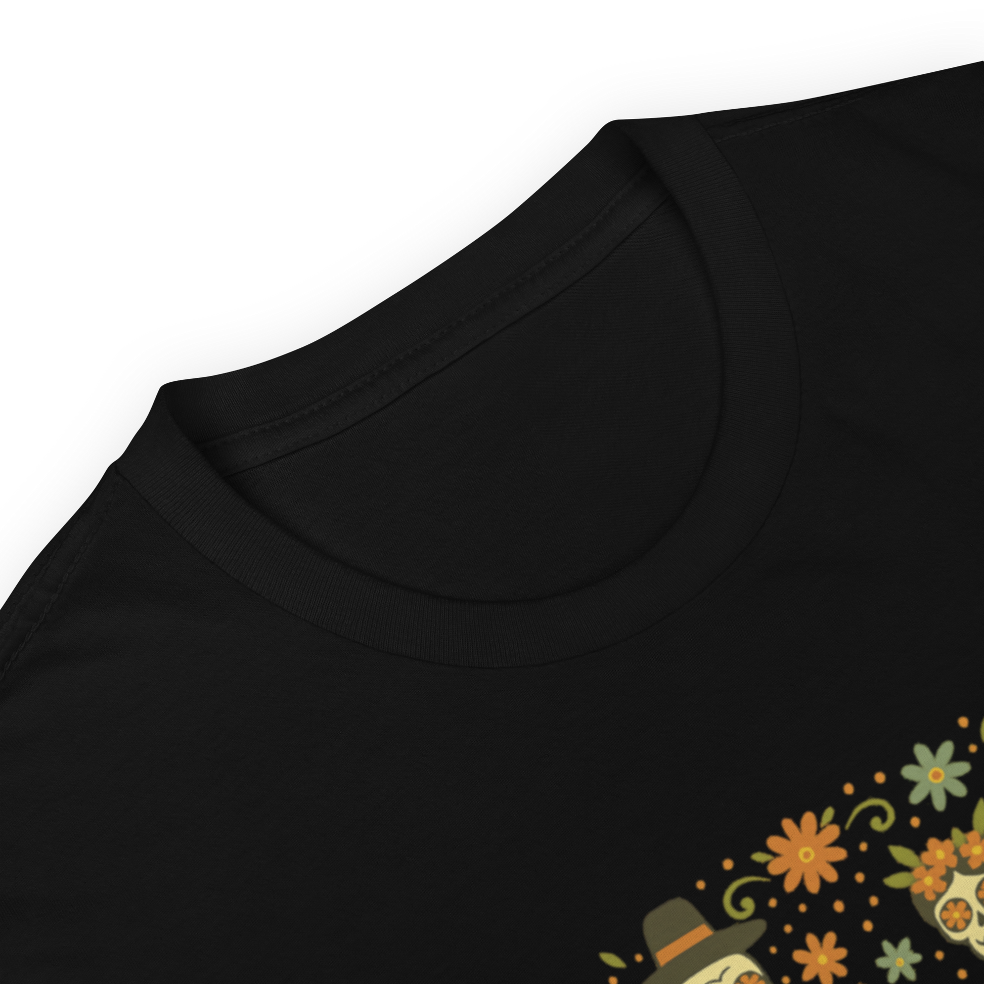 This is a zoom in of a black t-shirt with a Día de los Muertos–style illustration of a male and female skeleton holding hands, surrounded by marigolds, vines, and folk art patterns. The skeletons wear traditional black clothing, the man in a suit and hat, the woman with a floral crown with a red heart and leaves at the bottom and the text Creepy All Year. Rendered in warm tones of orange, green, and cream, symbolizing eternal love and remembrance