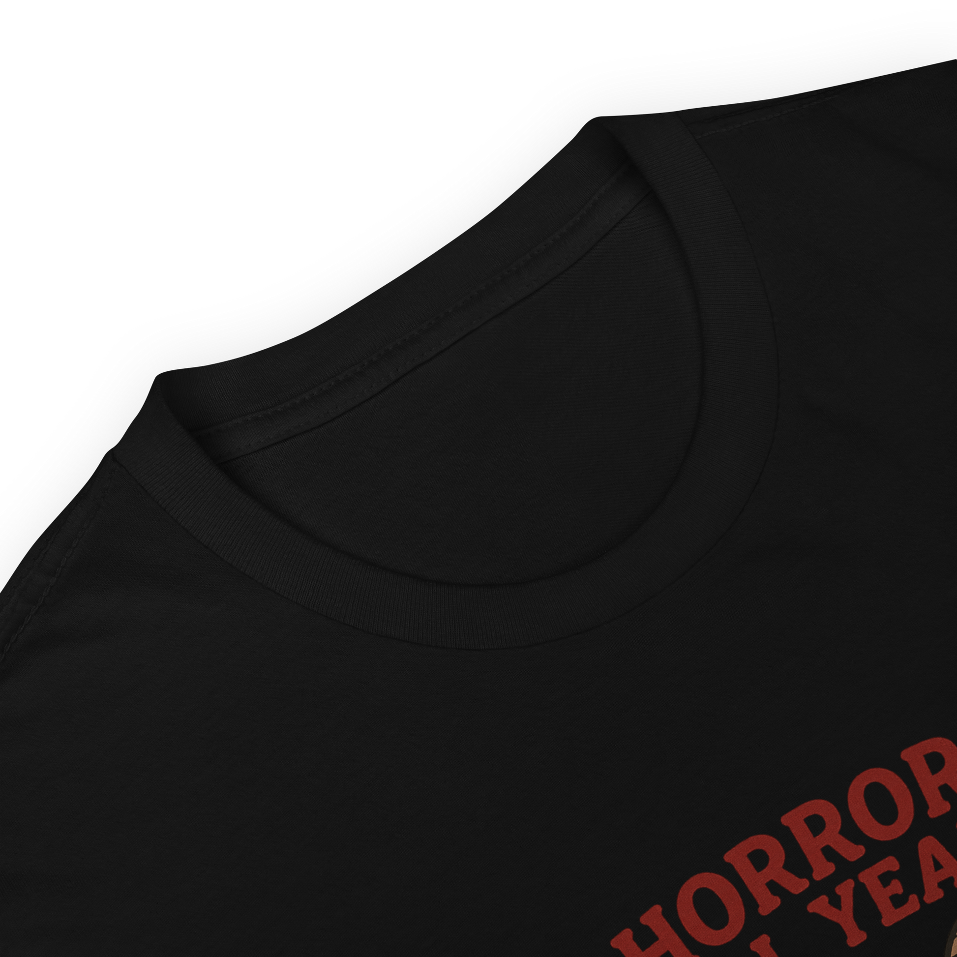 This is a zoom in of a black t-shirt with a cartoon illustration of a baby Baphomet goat with curved horns and a playful grin, wearing bright floral swim trunks while floating in a colorful inner tube. The character is set against a light background with the bold text “Horror All Year” above in red letters