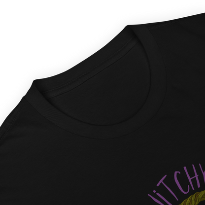 This is a zoom in of a black t-shirt with a design of a hand-drawn wreath made of moss-covered branches wraps around a glowing sun. The wreath is decorated with purple and blue flowers, small amethyst and fluorite crystals, and strands of hanging moss. The words “Witchy” curve above the wreath and “All Year” sits on the bottom right 