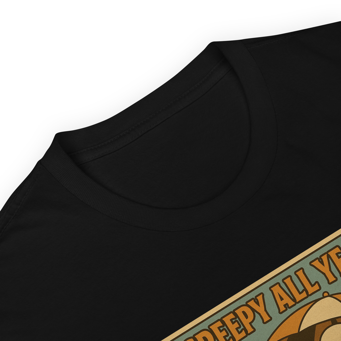 This is a zoom in of a black t-shirt with a retro-style illustration of a grinning skeleton lounging on a beach chair under an orange umbrella. The skeleton is holding a pumpkin-shaped drink cup with a straw and relaxing by the ocean, with a bright sun in the sky and a life preserver in the sand. The words “Creepy All Year” appear boldly at the top