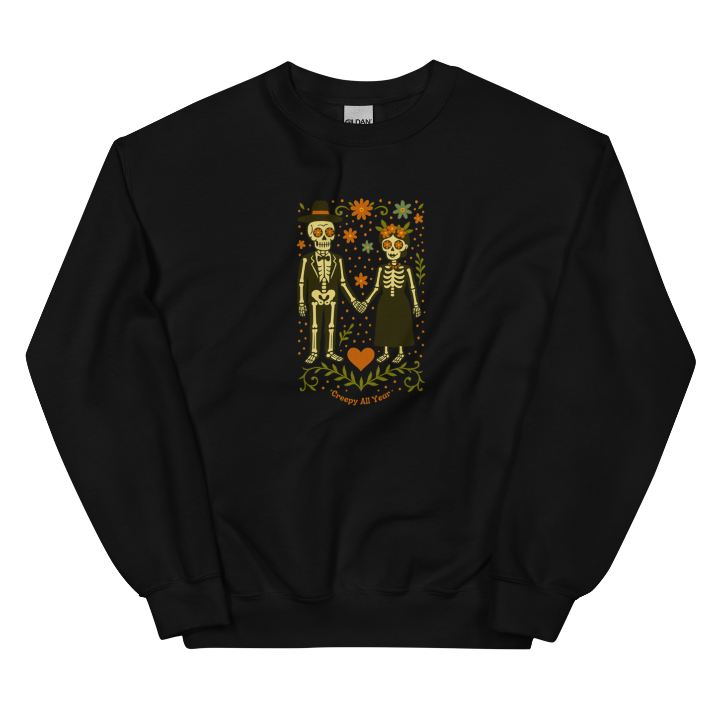 This is a black sweatshirt with a Día de los Muertos–style illustration of a male and female skeleton holding hands, surrounded by marigolds, vines, and folk art patterns. The skeletons wear traditional black clothing, the man in a suit and hat, the woman with a floral crown with a red heart and leaves at the bottom and the text Creepy All Year. Rendered in warm tones of orange, green, and cream, symbolizing eternal love and remembrance