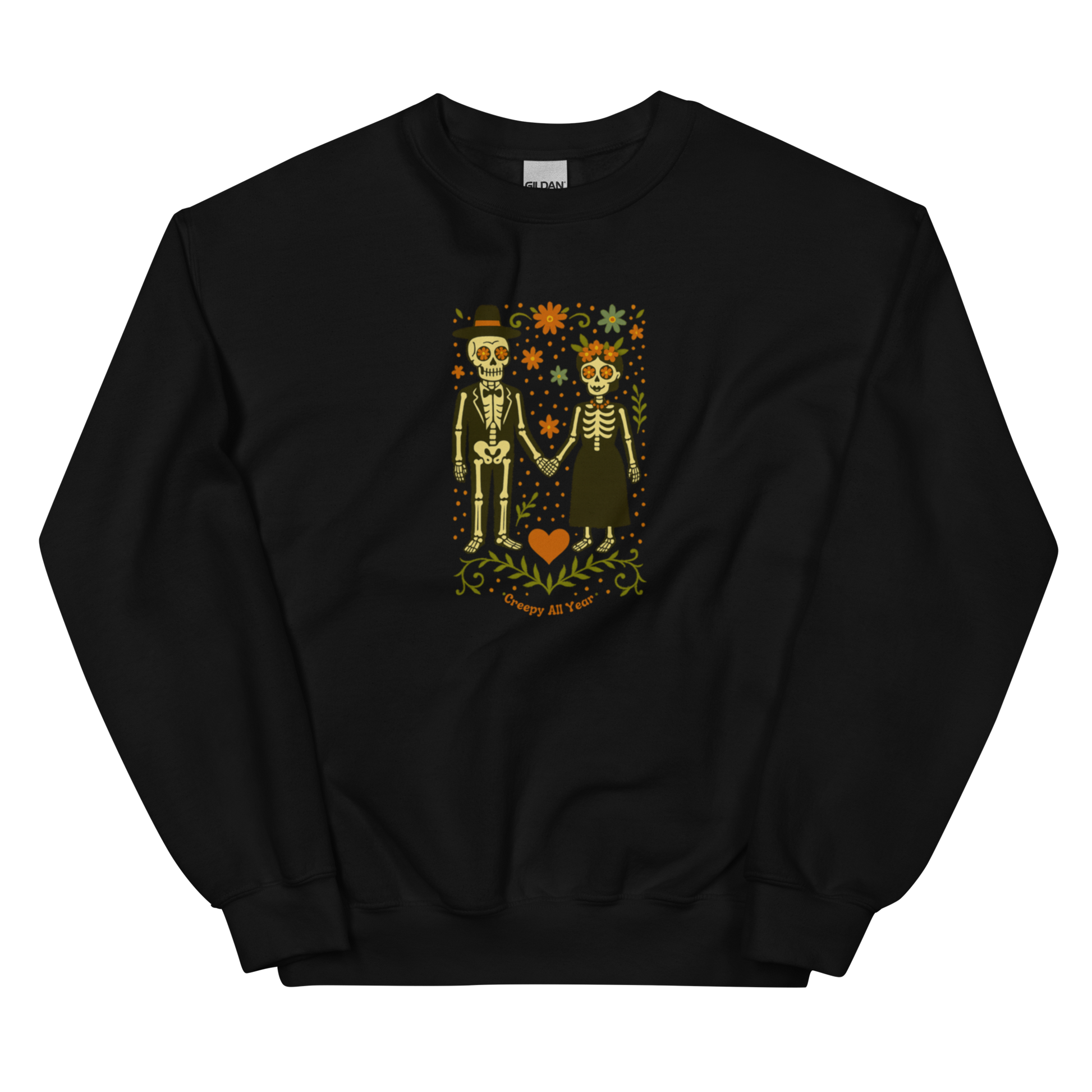 This is a black sweatshirt with a Día de los Muertos–style illustration of a male and female skeleton holding hands, surrounded by marigolds, vines, and folk art patterns. The skeletons wear traditional black clothing, the man in a suit and hat, the woman with a floral crown with a red heart and leaves at the bottom and the text Creepy All Year. Rendered in warm tones of orange, green, and cream, symbolizing eternal love and remembrance