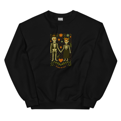 This is a black sweatshirt with a Día de los Muertos–style illustration of a male and female skeleton holding hands, surrounded by marigolds, vines, and folk art patterns. The skeletons wear traditional black clothing, the man in a suit and hat, the woman with a floral crown with a red heart and leaves at the bottom and the text Creepy All Year. Rendered in warm tones of orange, green, and cream, symbolizing eternal love and remembrance