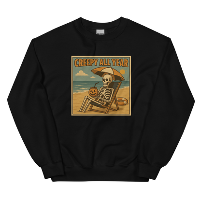 This is a black sweatshirt with a retro-style illustration of a grinning skeleton lounging on a beach chair under an orange umbrella. The skeleton is holding a pumpkin-shaped drink cup with a straw and relaxing by the ocean, with a bright sun in the sky and a life preserver in the sand. The words “Creepy All Year” appear boldly at the top