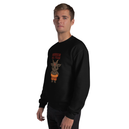 This is a man with blonde hair wearing a black sweatshirt with a cartoon illustration of a baby Baphomet goat with curved horns and a playful grin, wearing bright floral swim trunks while floating in a colorful inner tube. The character is set against a light background with the bold text “Horror All Year” above in red letters
