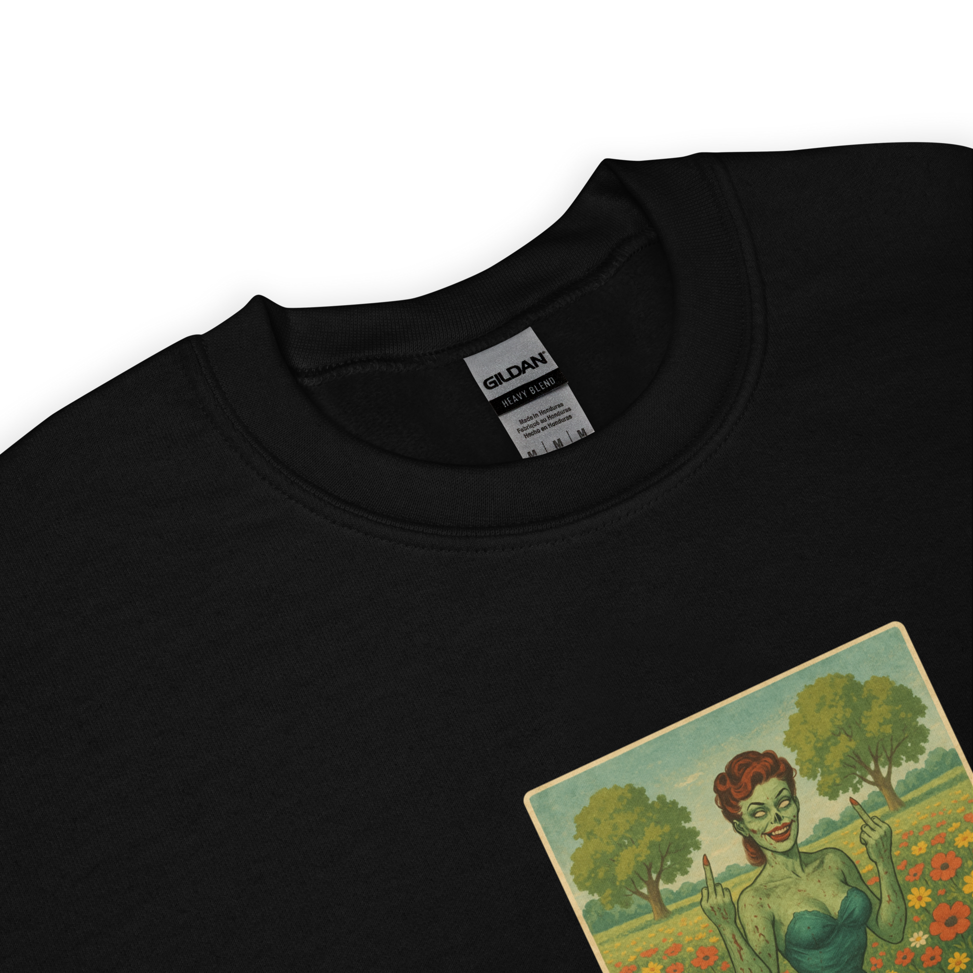 This is a zoom in of a black sweatshirt with a design illustration of a sassy zombie pinup girl standing in a floral field, wearing tattered lingerie and flipping off the viewer with both hands. She has green skin, vintage curls, and a bold attitude. The design blends horror and humor, with a pastel color palette and creepy cute vibes