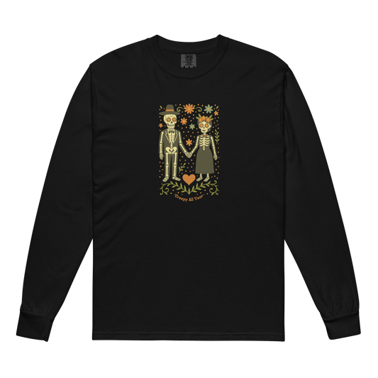 This is a black long sleeve shirt with a Día de los Muertos–style illustration of a male and female skeleton holding hands, surrounded by marigolds, vines, and folk art patterns. The skeletons wear traditional black clothing, the man in a suit and hat, the woman with a floral crown with a red heart and leaves at the bottom and the text Creepy All Year. Rendered in warm tones of orange, green, and cream, symbolizing eternal love and remembrance