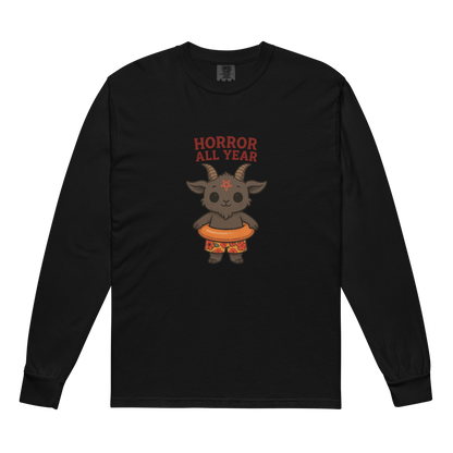 This is a black long sleeve shirt with a cartoon illustration of a baby Baphomet goat with curved horns and a playful grin, wearing bright floral swim trunks while floating in a colorful inner tube. The character is set against a light background with the bold text “Horror All Year” above in red letters
