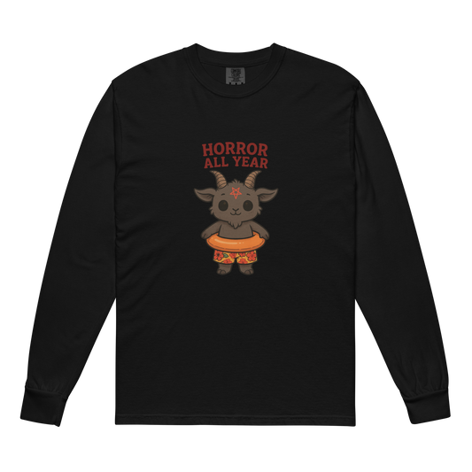 This is a black long sleeve shirt with a cartoon illustration of a baby Baphomet goat with curved horns and a playful grin, wearing bright floral swim trunks while floating in a colorful inner tube. The character is set against a light background with the bold text “Horror All Year” above in red letters
