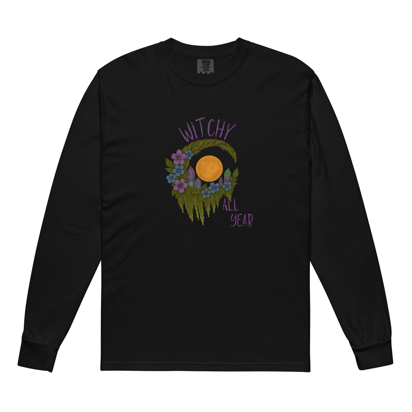 This is a black long sleeve shirt with a design of a hand-drawn wreath made of moss-covered branches wraps around a glowing sun. The wreath is decorated with purple and blue flowers, small amethyst and fluorite crystals, and strands of hanging moss. The words “Witchy” curve above the wreath and “All Year” sits on the bottom right 