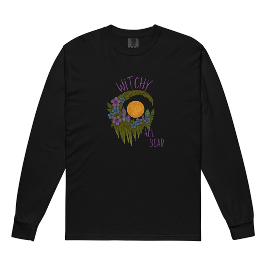 This is a black long sleeve shirt with a design of a hand-drawn wreath made of moss-covered branches wraps around a glowing sun. The wreath is decorated with purple and blue flowers, small amethyst and fluorite crystals, and strands of hanging moss. The words “Witchy” curve above the wreath and “All Year” sits on the bottom right 